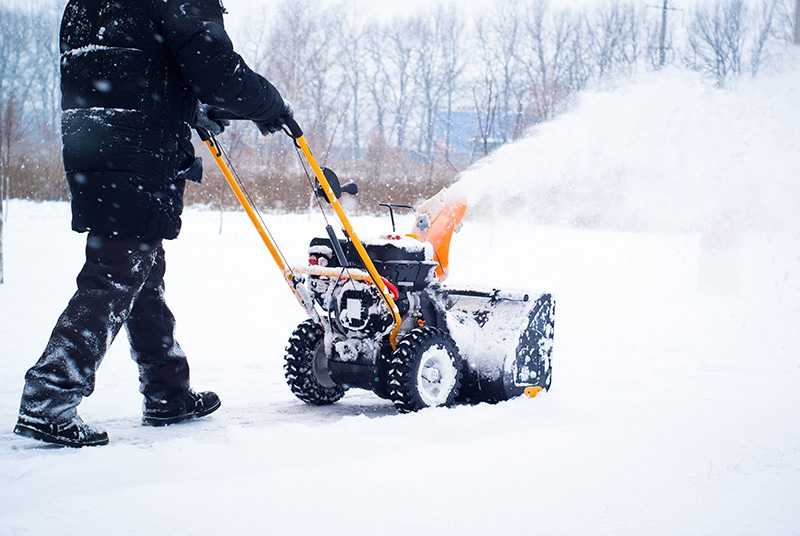 A man cleans snow from sidewalks with snowblower. Colonial Lawn and Garden